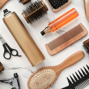 Auf dem weißen Marmortisch liegen Friseurutensilien: Kämme, Haarspray, Scheren und Haarpflegemittel in einer orangefarbenen Flasche