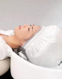 Person beim Entspannen mit Dampfkappe während der Haarpflegebehandlung im Friseursalon.